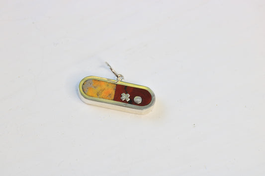 sterling silver pill shaped charm inlaid with bumblebee jasper and dot's plume on a white background