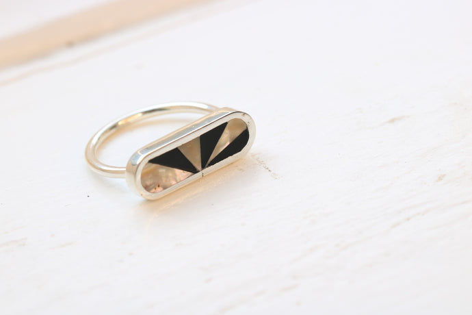 sterling silver ring inlaid with abalone and black petrified wood in a fan pattern sitting on white background